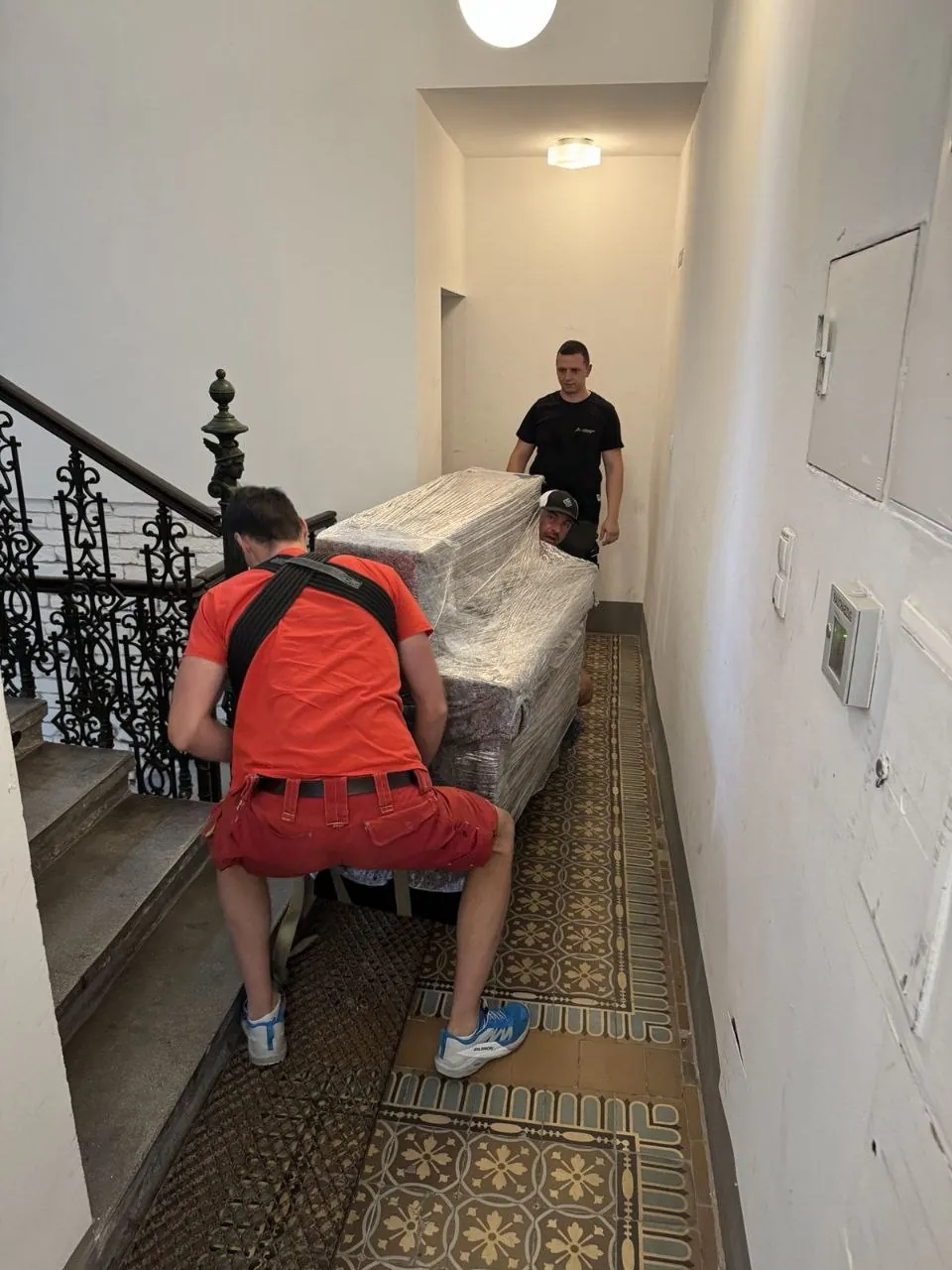 Vier Nomaden Umzug Mitarbeiter tragen einen verpackten Flügel durch einen Altbau-Gang