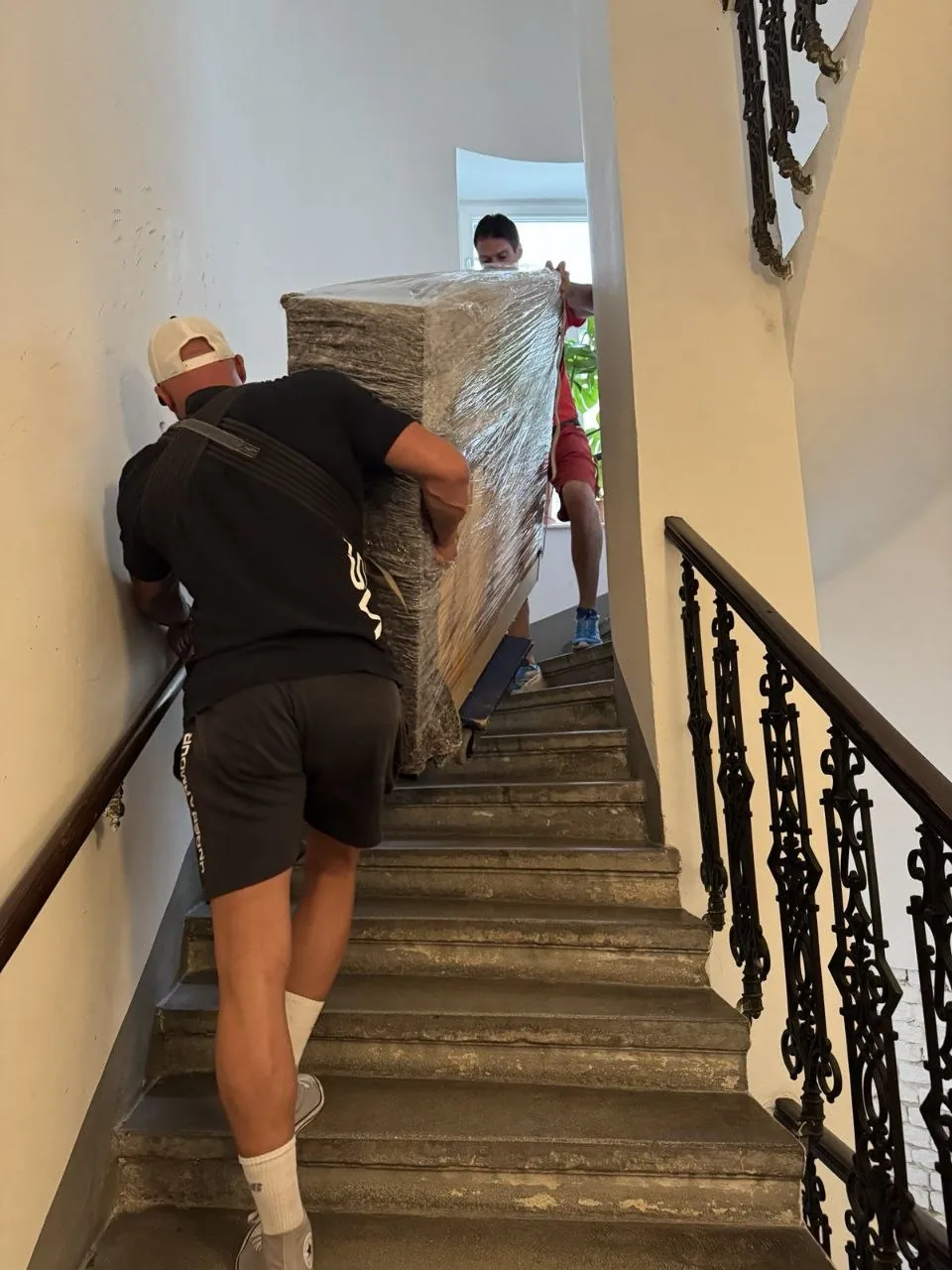 Nomaden Umzug Team trägt ein Klavier mit Gurten durch ein Wiener Altbau-Stiegenhaus